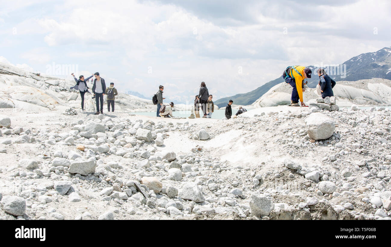 Los turistas en el glaciar del Ródano en Suiza. Después de un invierno con cantidades récord de nieve, la mayoría de los que se había ido cuando este imae fue tomada el 14 de julio de 2018, exponiendo el hielo más oscuro. Mientras la nieve brillante es una parábola de la energía del sol, el hielo oscuro absorbe la energía, acelerando el derretimiento del glaciar. El color y la oscuridad de hielo glaciar varían en todo el mundo, dependiendo de la acumulación de la contaminación, la edad del hielo, las partículas recogidas por el hielo y por microorganismos en el hielo. El hielo glaciar es, sin embargo, raramente blancas como la nieve. Con inviernos más cortos y desapareciendo la nieve cove Foto de stock