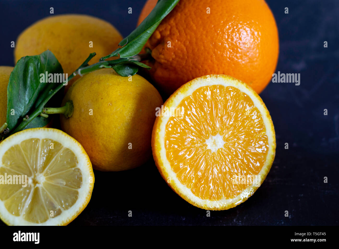 Las Naranjas y los limones con todo y frutas cortadas sobre un fondo oscuro Foto de stock