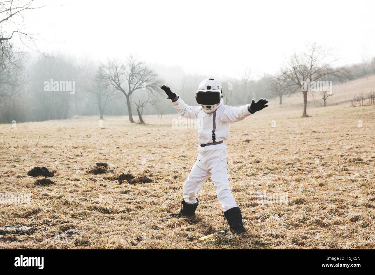 Boy vestidas de blanco traje espacial está posando al aire libre en medio de un prado con gafas de realidad virtual Foto de stock