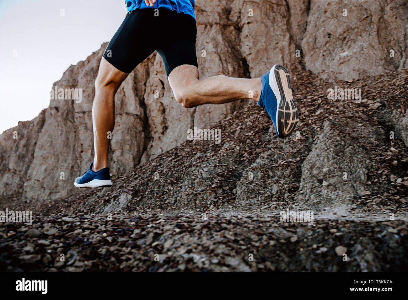 Piernas hombre runner corriendo en piedras de montaña trail Foto de stock