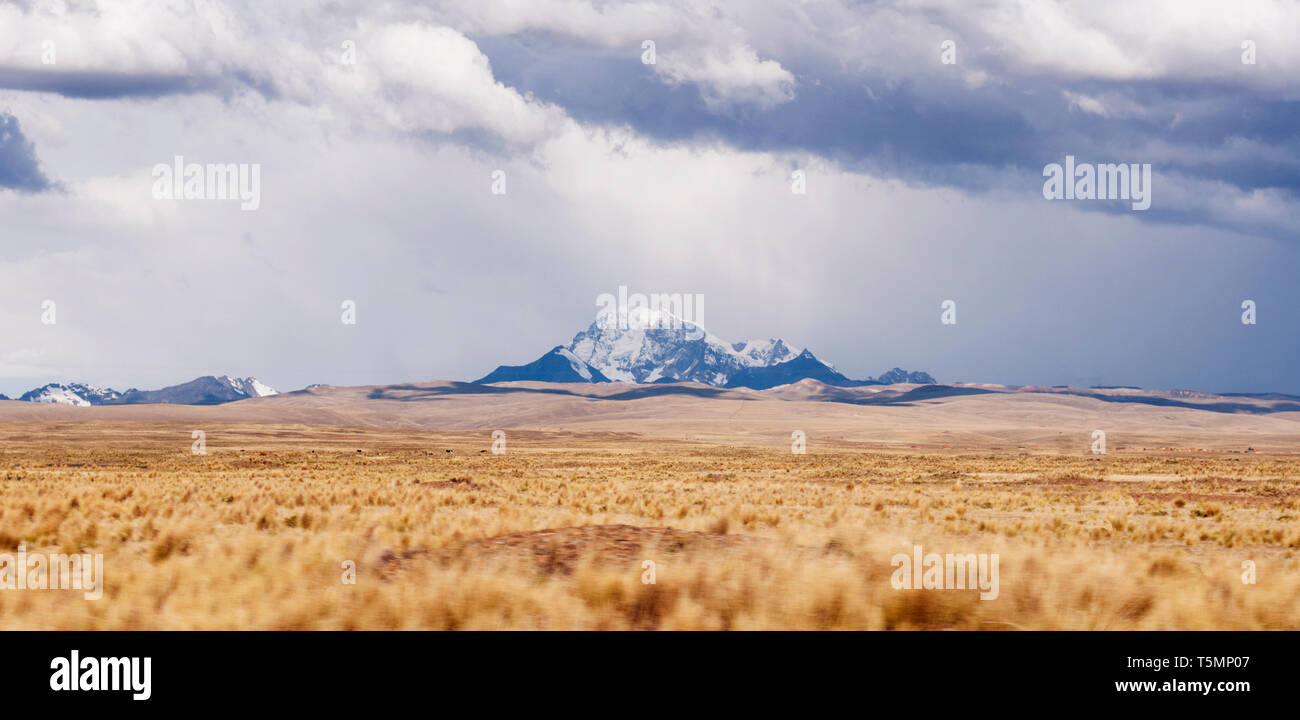 Cuando el cielo está nublado en altas montañas panorámicas en Bolivia con hierba seca, de color naranja en la parte delantera. Foto de stock