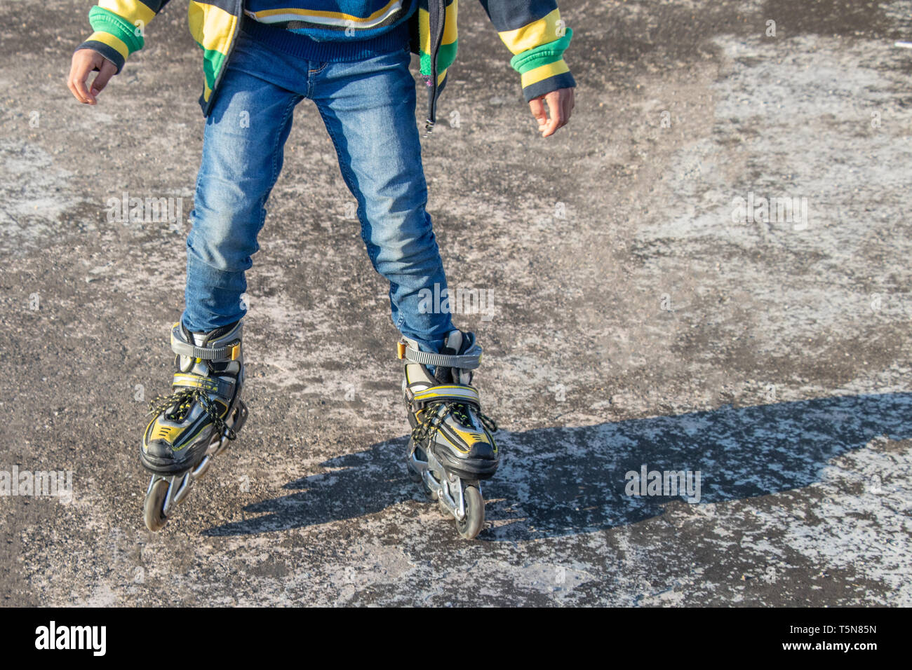 Niño patinando sobre piso de concreto en un brillante día soleado Foto de stock