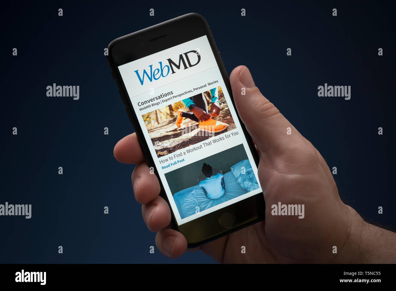 Un hombre mira el iPhone que muestra el logotipo de WebMD (uso Editorial solamente). Foto de stock