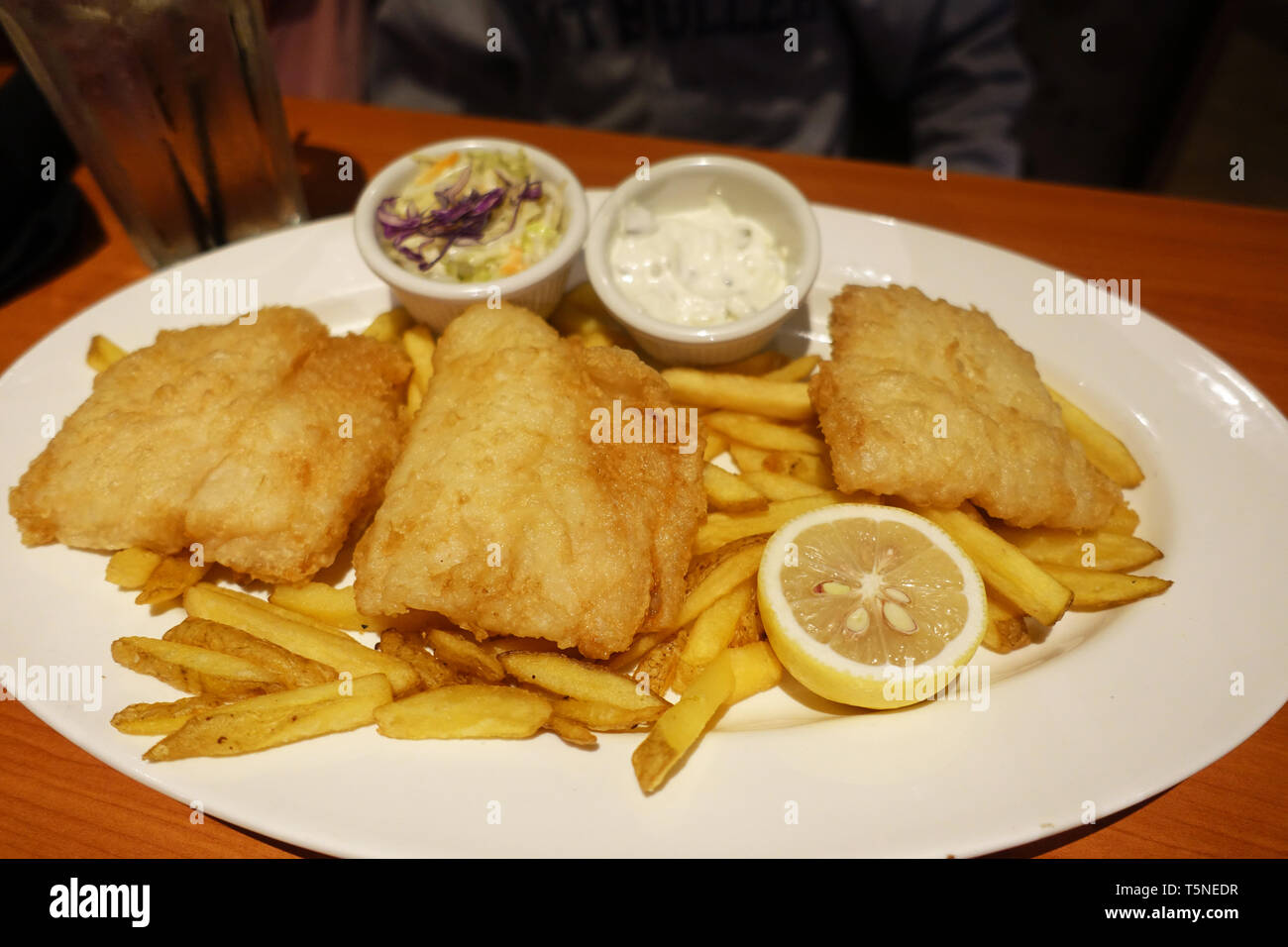 El pescado con patatas fritas y salsa tártara, coleslaw y limón sobre placa blanca. Foto de stock