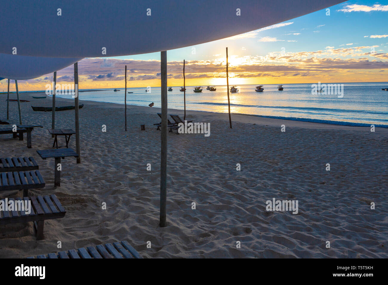 Playa con sillas de madera y una tienda de barcos y la puesta de sol en el fondo.Concepto de vacaciones, paz y relajación. Ponta do Corumbau, Bahia, Brasil Foto de stock