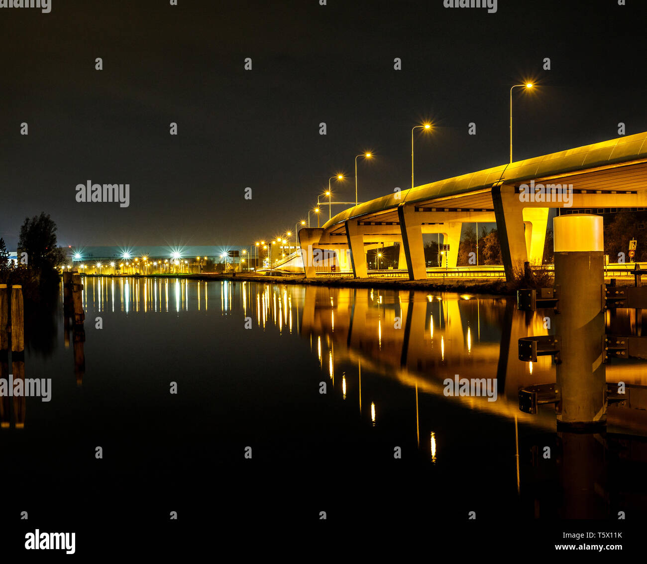 Enorme puente con luces junto al mar con vistas al horizonte de la ciudad en la espalda en la noche Foto de stock