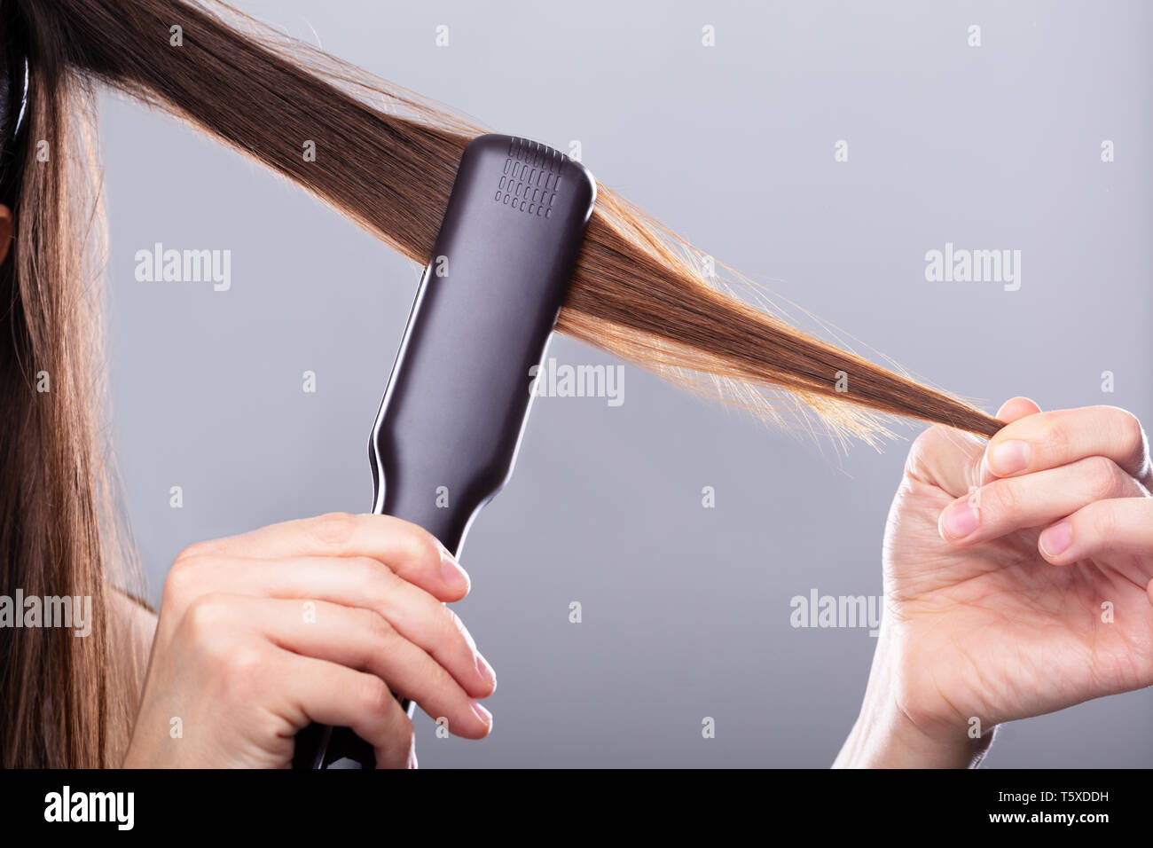 Close-up de mujer cabello alisado con plancha contra el fondo gris  Fotografía de stock - Alamy