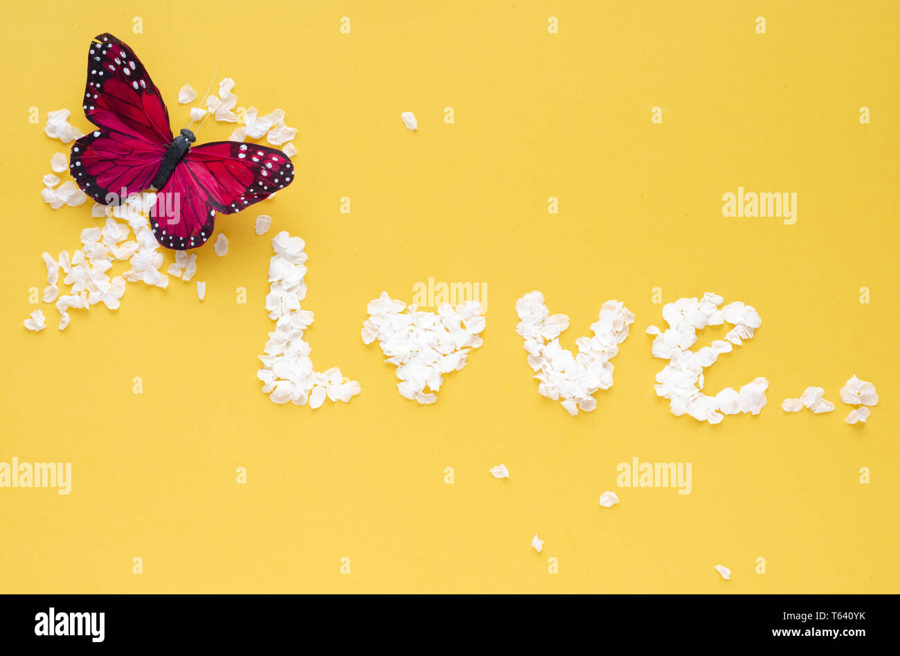 Palabra amor con pétalos de flores blancas sobre fondo amarillo. Con mariposas decorativas. Foto de stock