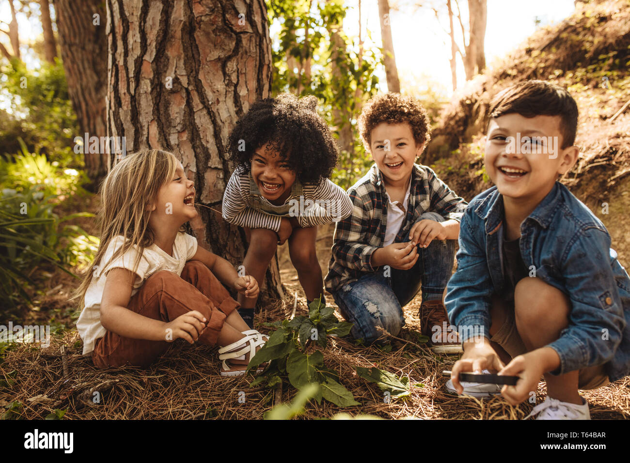 Grupo de lindos hijos sentados juntos en el bosque y mirando a la cámara. Cute niños jugando en los bosques. Foto de stock