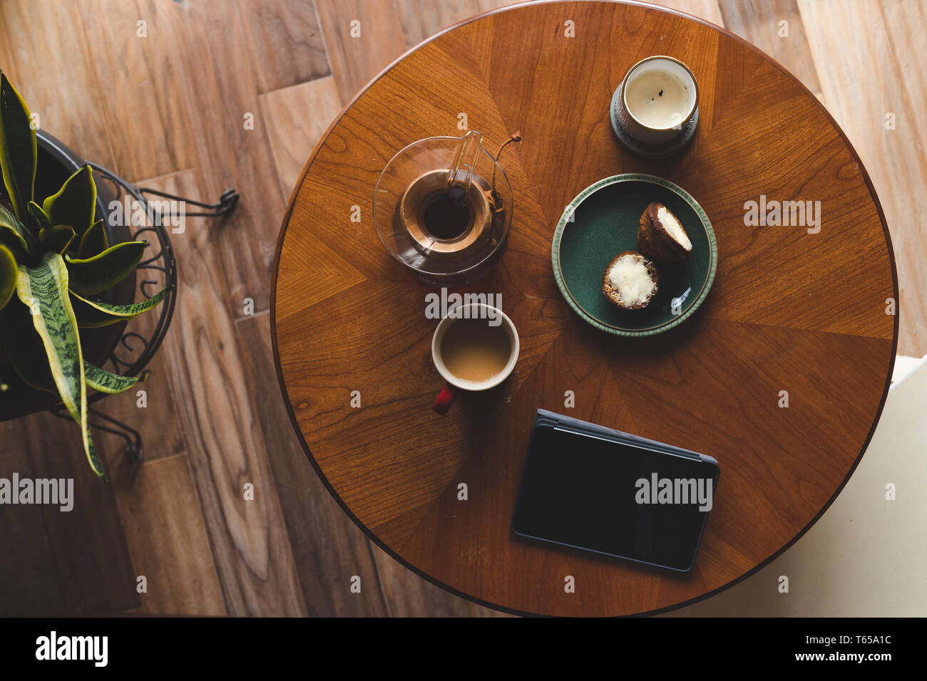 Un disparo de arriba hacia abajo de la moderna sala de estar y mesa de café con una taza de café, libro, tabletas y un panecillo. Foto de stock