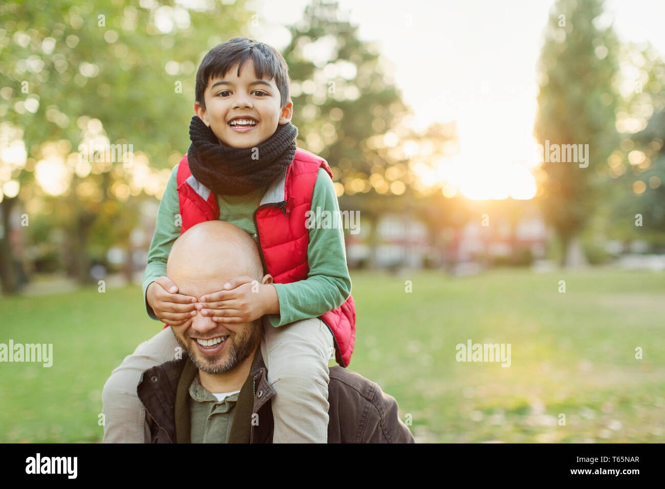 Retrato juguetón hijo cabalgando sobre los hombros de los padres en el parque de otoño Foto de stock