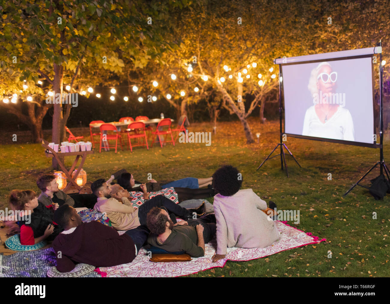 Amigos viendo la película en pantalla de proyección en el patio Foto de stock