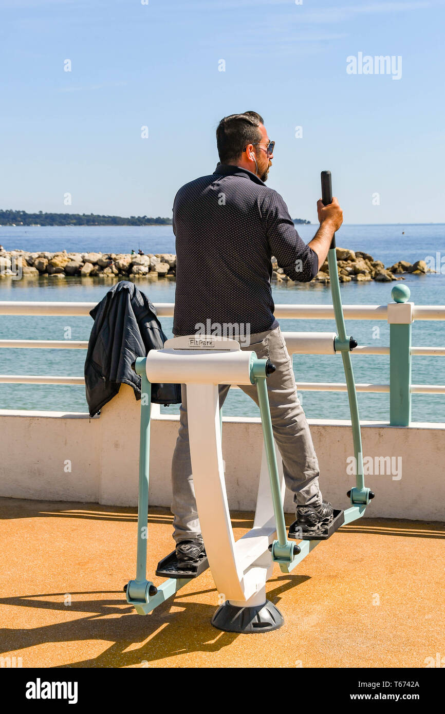 CANNES, Francia - Abril 2019: persona usando una máquina de entrenamiento cruzado en un gimnasio al aire libre en el paseo marítimo de Cannes Foto de stock