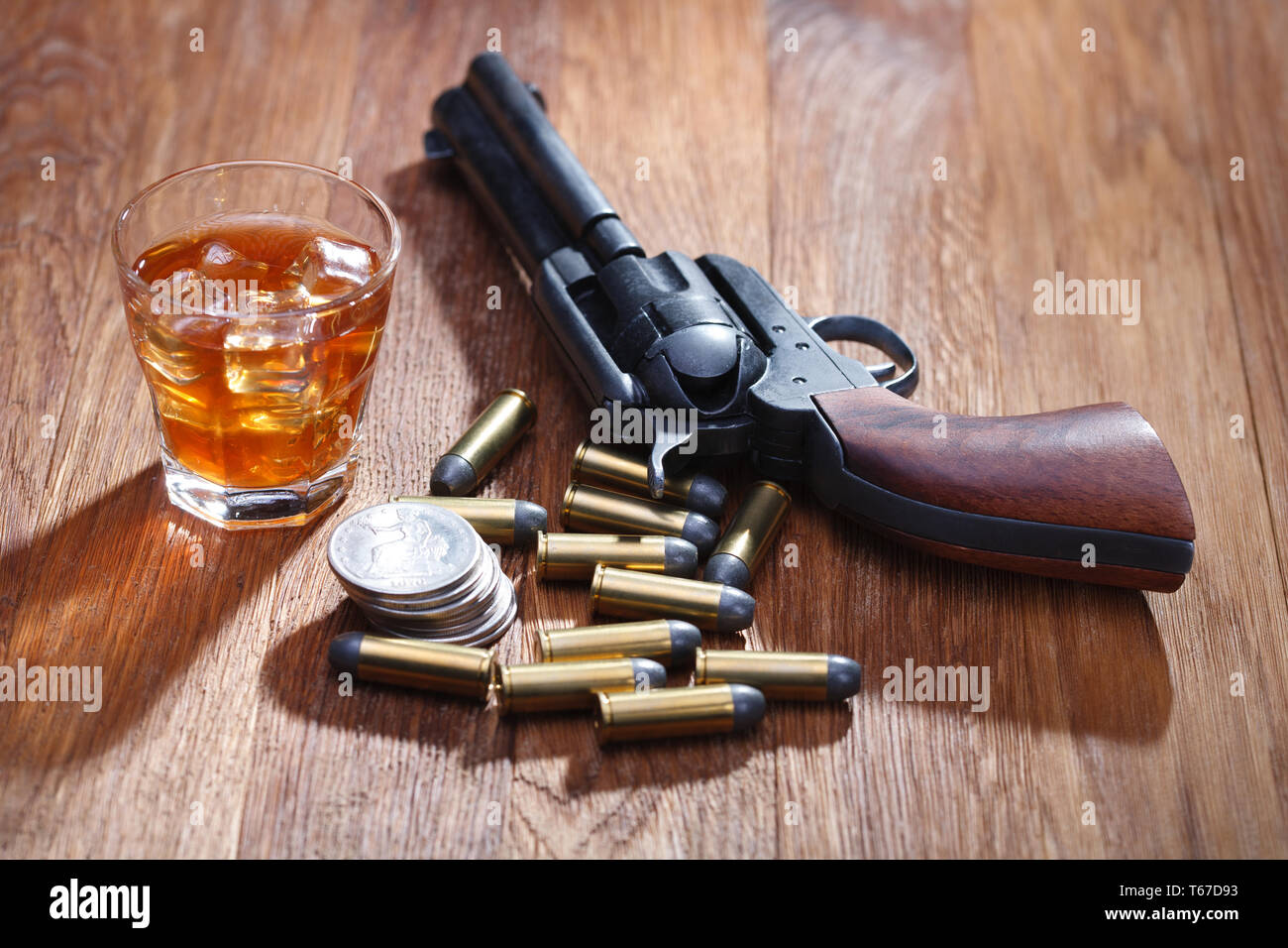 Wild West revolver y municiones con un vaso de whisky con hielo y en dólar  de plata vieja mesa de bar de madera Fotografía de stock - Alamy