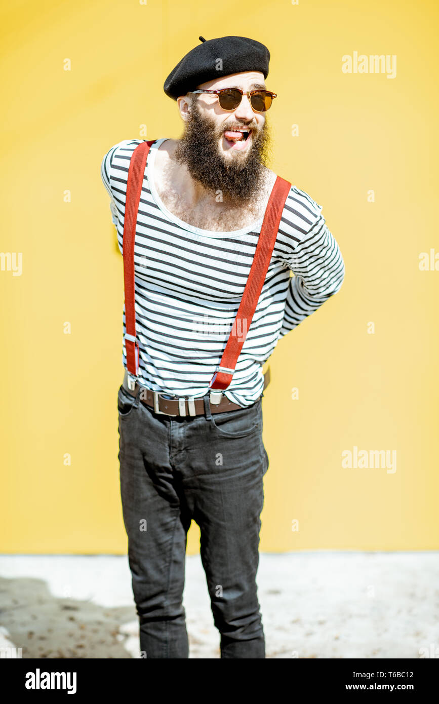 Retrato de un hombre barbado elegante vestido con camisa a rayas, tirantes  y sombrero sobre fondo amarillo en el exterior Fotografía de stock - Alamy
