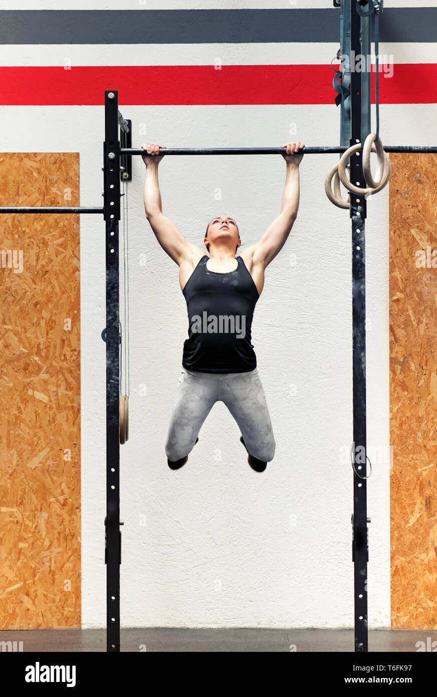Colocar musculares fuertes chica joven atleta haciendo pull-ups en un bar durante su entrenamiento en una vista frontal completa dentro de un gimnasio profesional Foto de stock