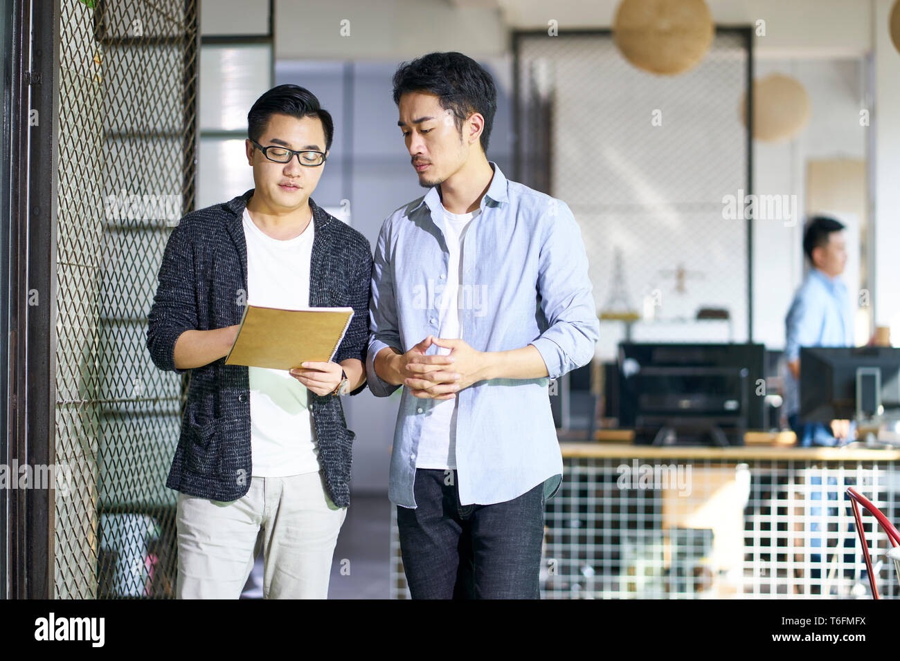 Dos jóvenes compañeros hablando de negocios asiáticos mientras camina en la oficina. Foto de stock