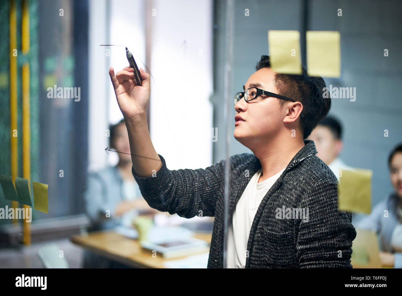 El hombre de negocios joven asiático dibujar un diagrama sobre vidrio durante una reunión en la oficina. Foto de stock