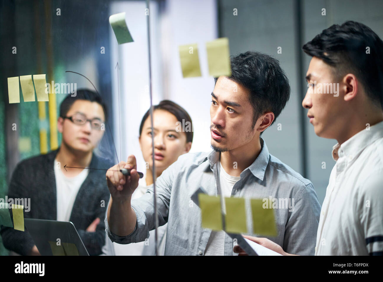 Joven empresario asiático de pequeña empresa dibujar un diagrama sobre vidrio durante el taller de equipo de oficina en debatir y formular estrategias de negocio. Foto de stock
