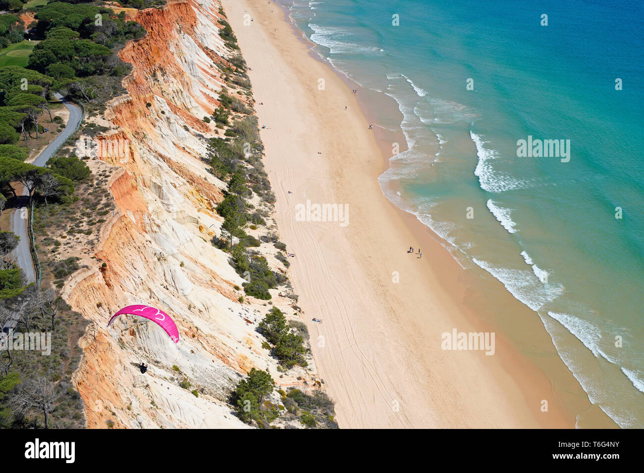 VISTA AÉREA. Parapente utilizando la brisa marina para elevarse a lo largo de un colorido acantilado junto al mar. Praia da Falésia, Albufeira, Algarve, Portugal. Foto de stock