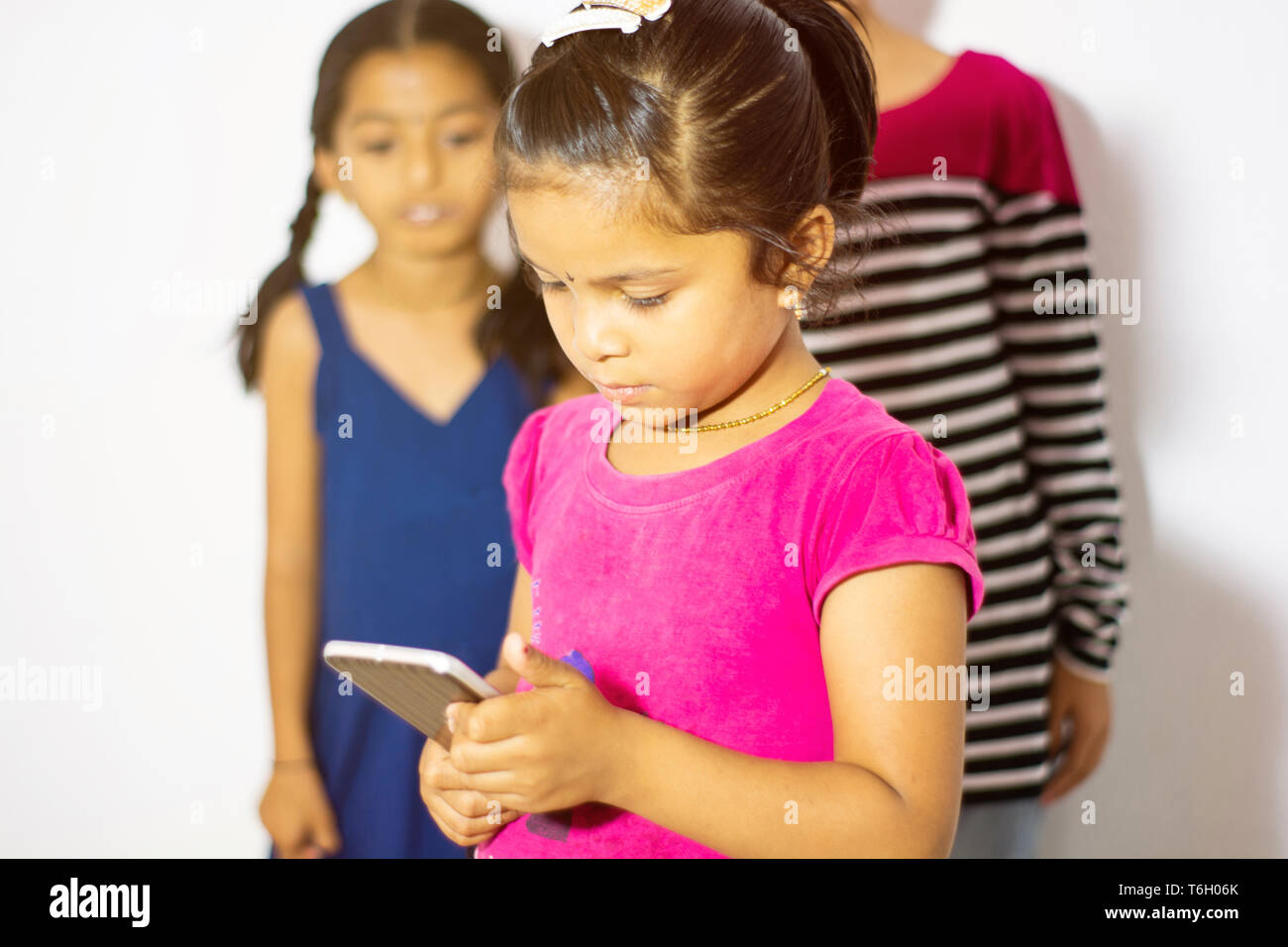 Lindo chiquillo indio utilizando dispositivos móviles y dos niños mirando el teléfono desde su detrás Foto de stock