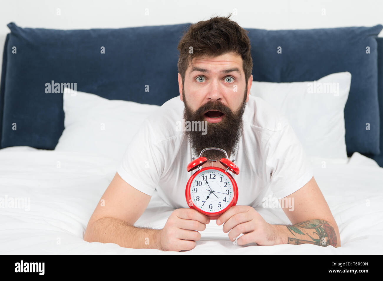 Despertarse temprano da más tiempo para prepararse y ser oportuna. Hipster  hombre barbado acostada en la cama con el despertador. Hora de despertar.  ¿Por qué usted debe levantarse temprano por las mañanas.