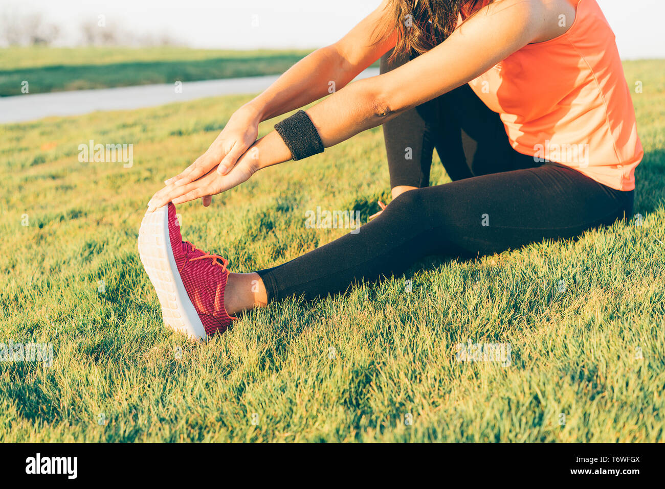 Mujer joven corredora estirar las piernas antes de ejecutar en un parque. Cerrar el Athletic y saludable niña vestidos de blanco y rosa sneakers. Foto de stock