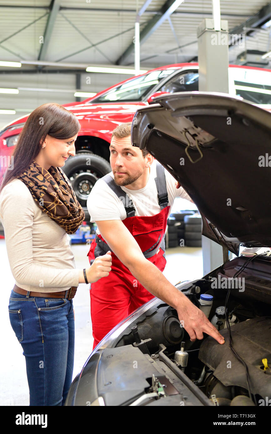 Servicio de atención al cliente en un garaje - mecánico y mujer discutir la reparación de un vehículo Foto de stock
