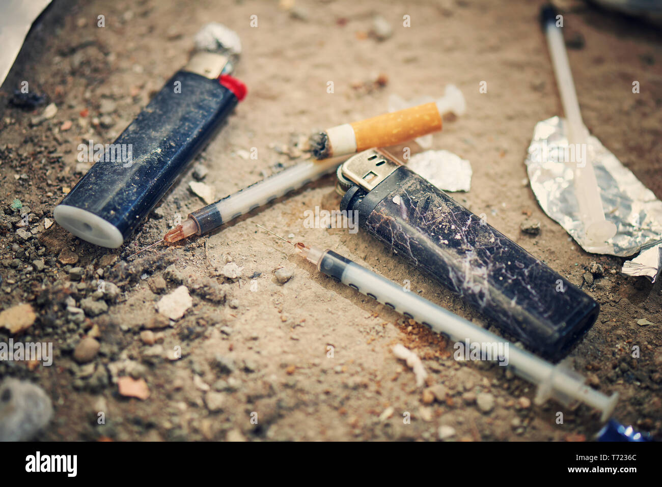 Jeringa usada en la tierra - Las adicciones equipo. La heroína, la jeringa y encendedor de cigarrillos - Concepto de drogadicción Foto de stock