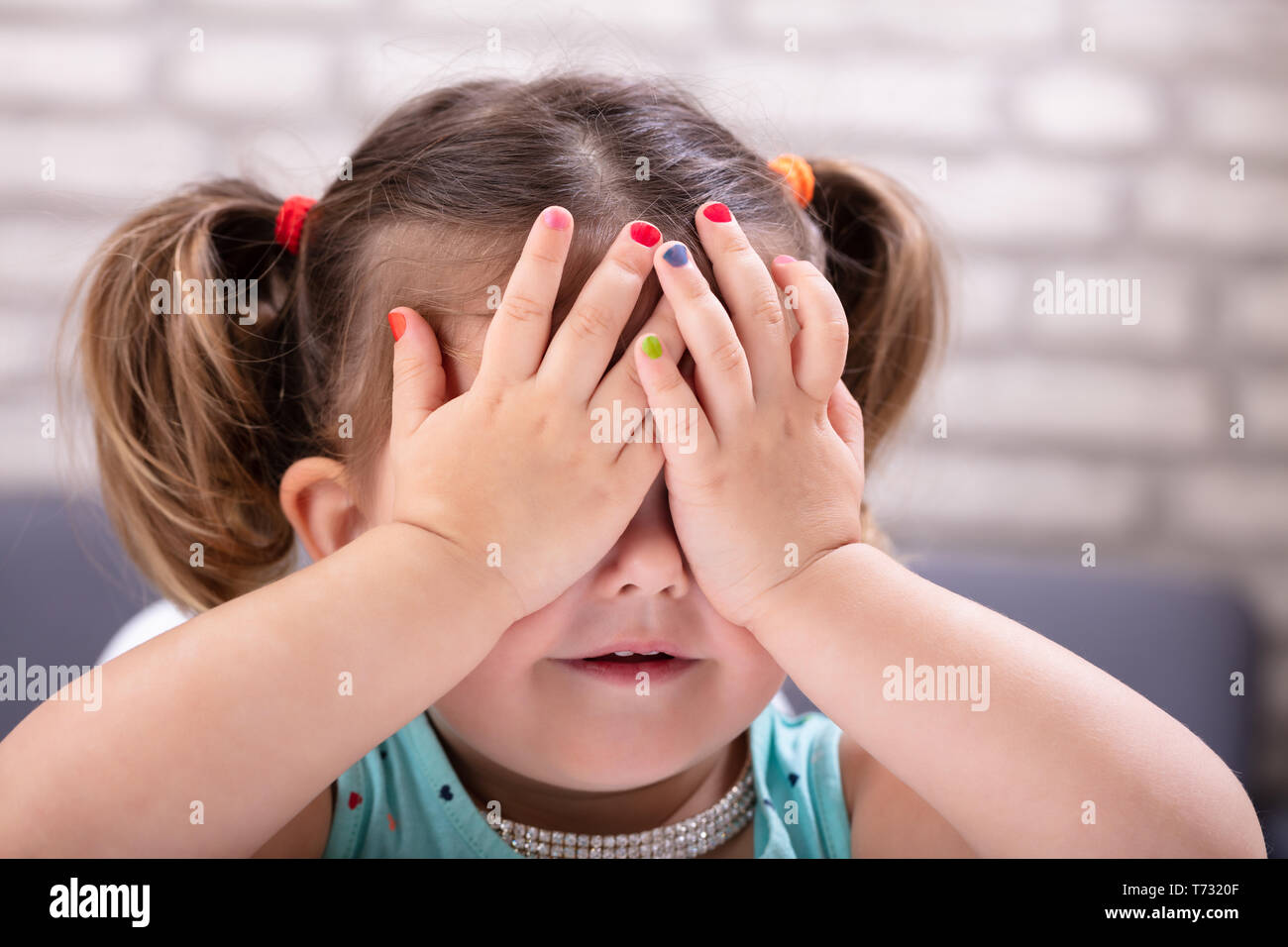 Vista frontal de la linda chica cubre sus ojos con la mano mostrando coloridos esmaltes de uñas Foto de stock