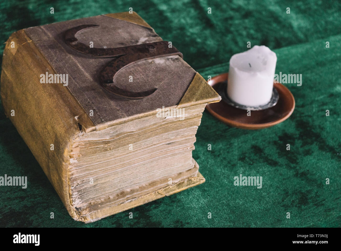 Antiguo libro pesado y vela en la mesa medieval, vista diagonal Foto de stock