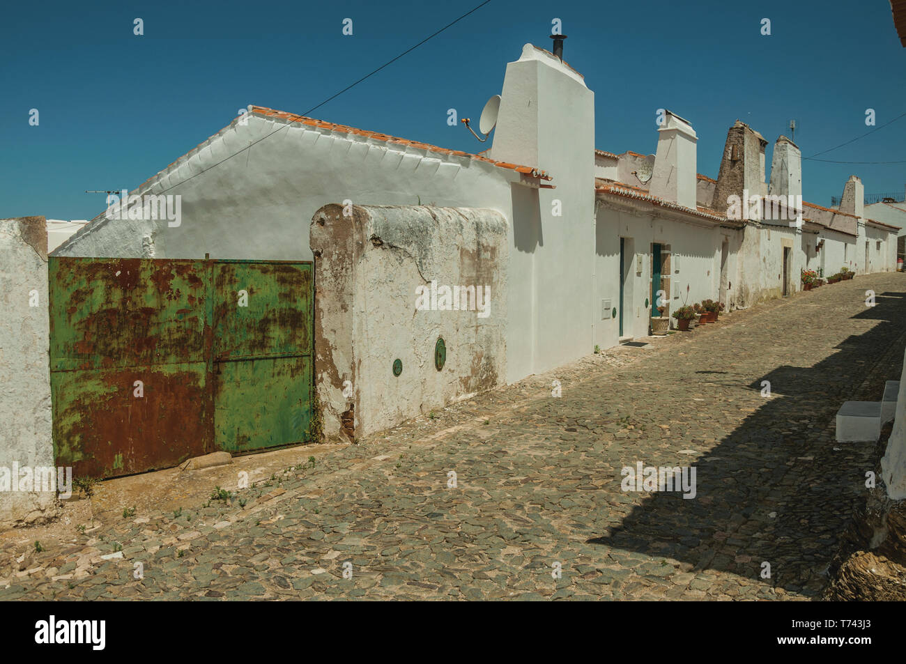 Pared Blanca humildes casas con puertas de garaje de hierro en un día  soleado, en una calle de Evoramonte. Una pequeña parroquia civil  fortificada con un castillo antiguo en Portugal Fotografía de