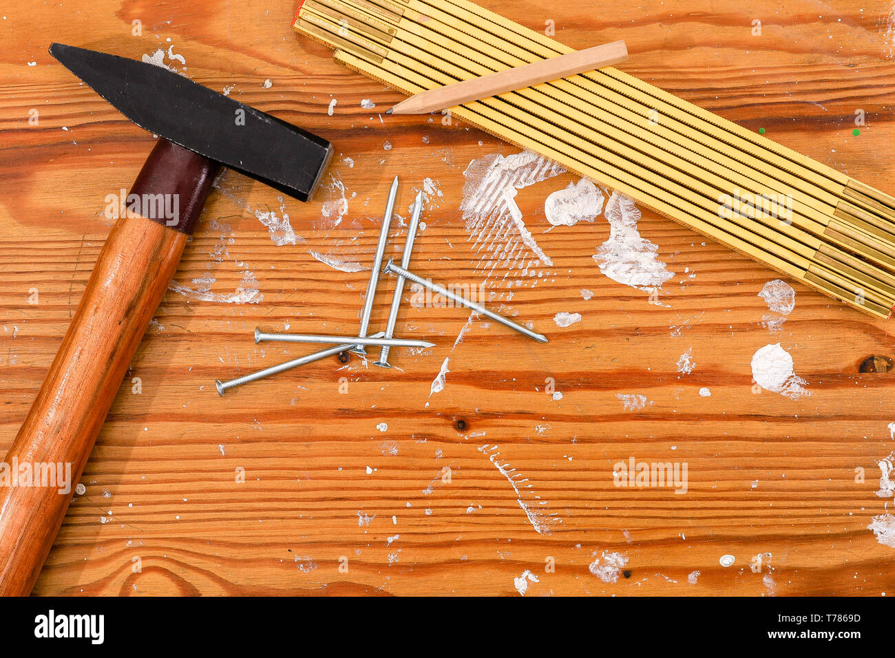 Martillo, regla plegable y uñas sobre un tablero de madera manchada. Foto de stock