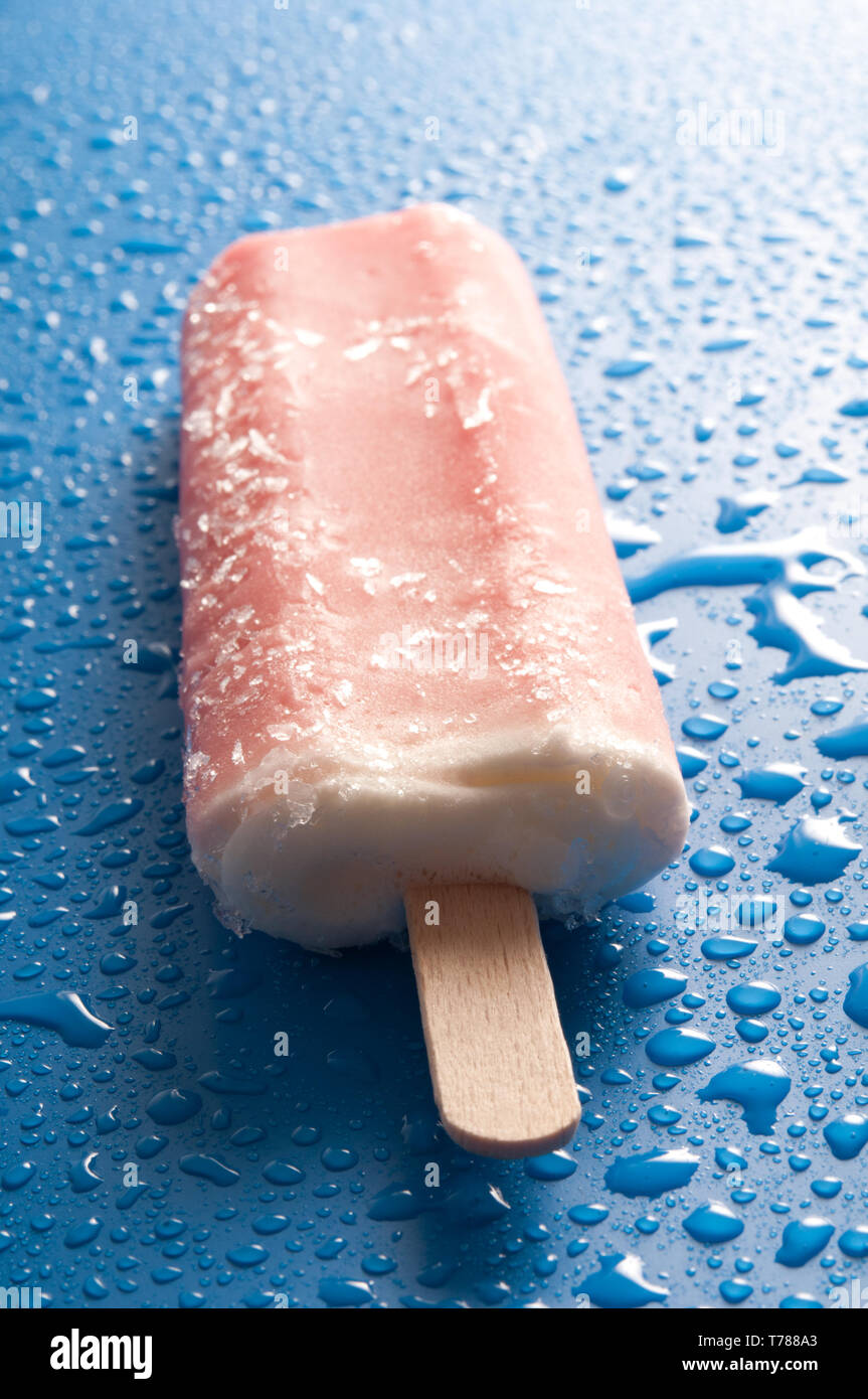 Máquina de paleta de helado de naranja o cubito de hielo sobre un fondo azul con gotas de agua Foto de stock
