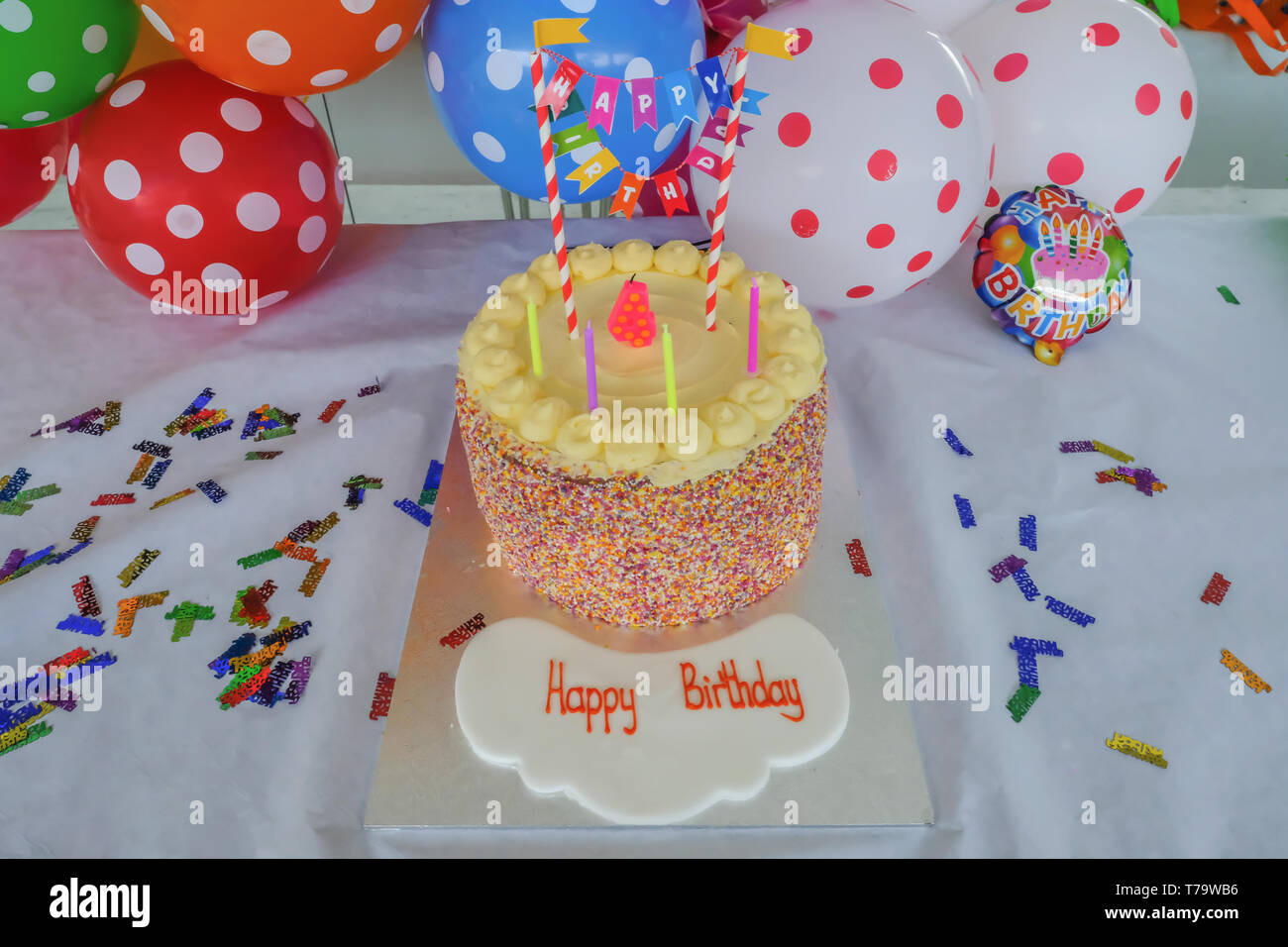 Pastel de cumpleaños de niños con velas set delante de coloridos globos aerostáticos irregular. Listo para un partido con un feliz cumpleaños escrito en primer plano. Foto de stock
