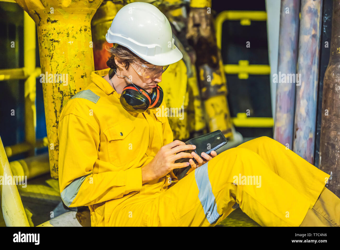 Joven en un amarillo uniforme de trabajo, gafas y casco en entorno  industrial,plataforma de petróleo o gas licuado planta busca en su  billetera vacía. ¿ Fotografía de stock - Alamy