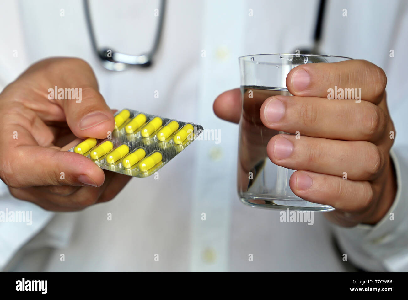 Doctor celebración píldoras y un vaso de agua, terapeuta de administrarle el medicamento en blister con cápsulas de color amarillo. Concepto de prescripción médica, medicamentos Foto de stock