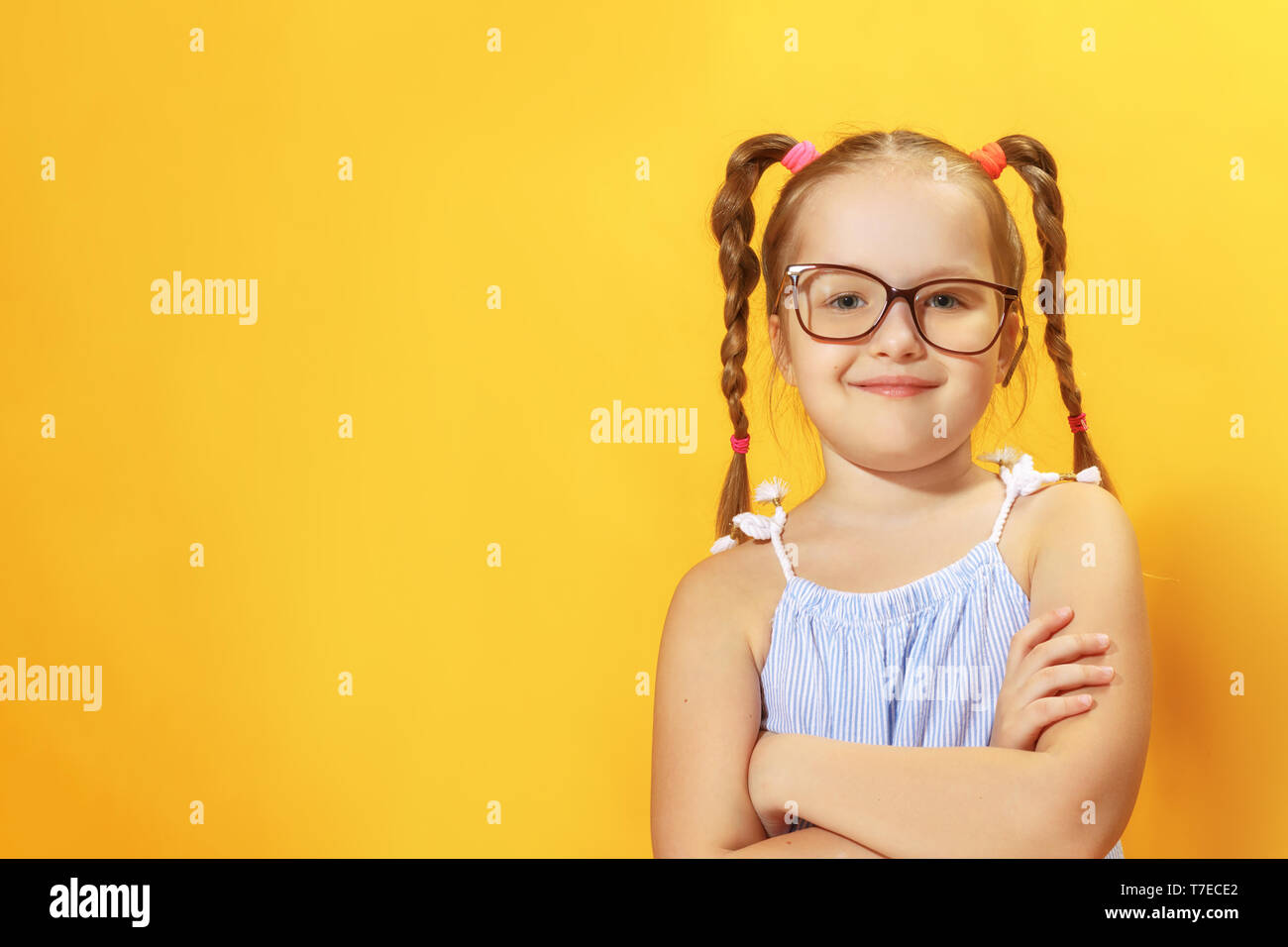 Retrato de una divertida niña de edad preescolar con gafas sobre un fondo amarillo. Foto de stock