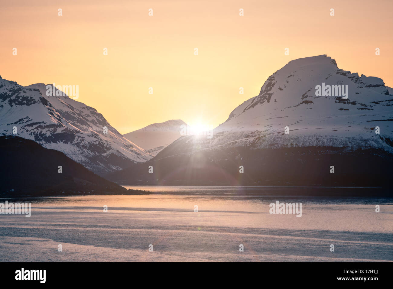 Montañas cubiertas de nieve y fjord al atardecer con efecto Destello de lente Foto de stock