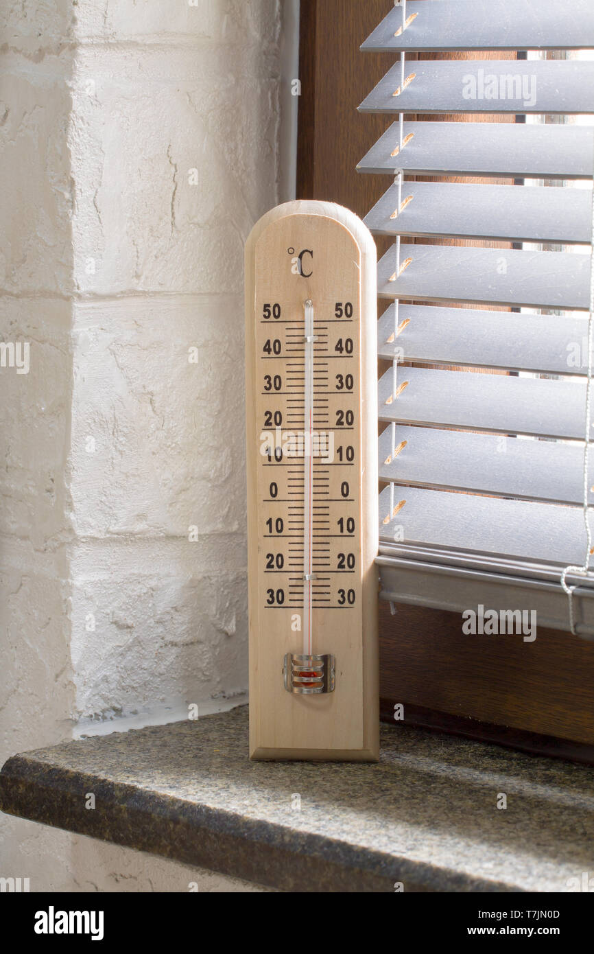 Un termómetro de madera con escala analógica midiendo la temperatura colocado cerca de la ventana Foto de stock
