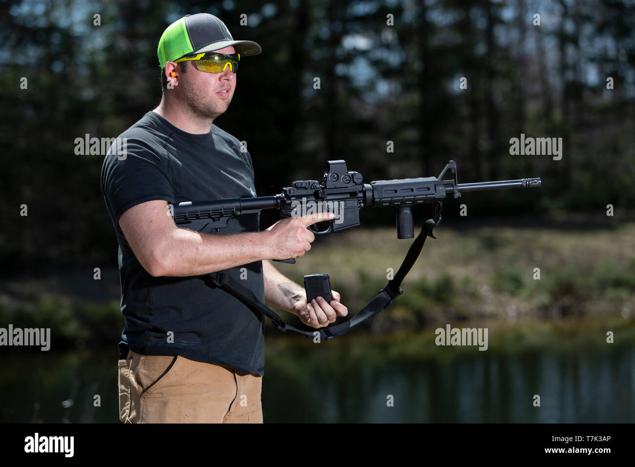 Un hombre sostiene un rifle deportivo moderno en una mano y la revista en la otra mano. Foto de stock