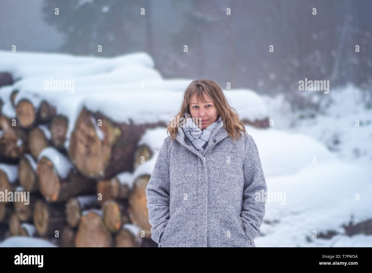 Una mujer rubia, de 40 años de edad está de pie en el paisaje invernal. Ella está sonriendo ante la cámara. La mujer viste un abrigo de lana gris claro y una bufanda. En el b Foto de stock