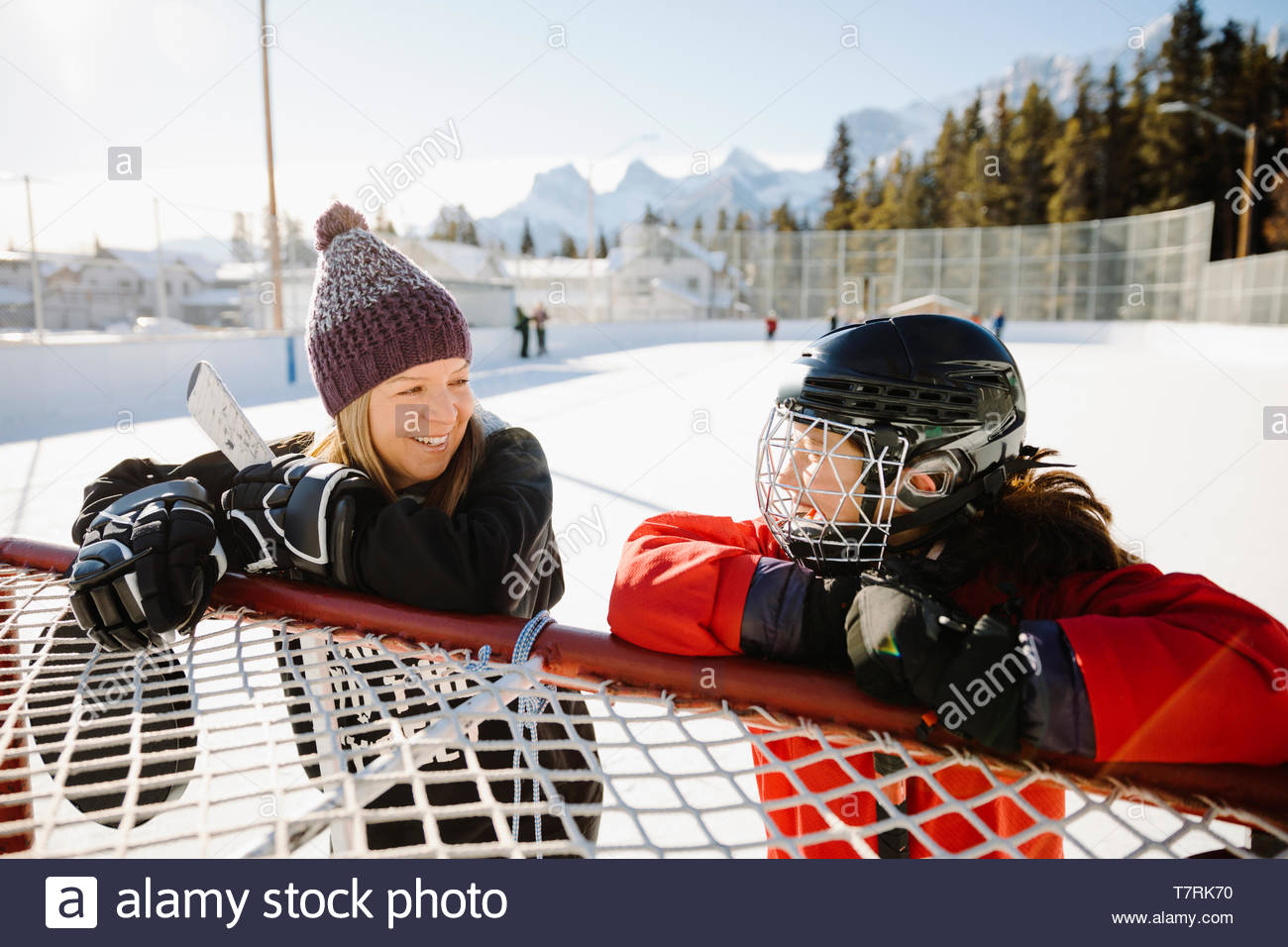 Feliz madre e hija jugar hockey sobre hielo al aire libre, tomando un descanso en el objetivo Foto de stock