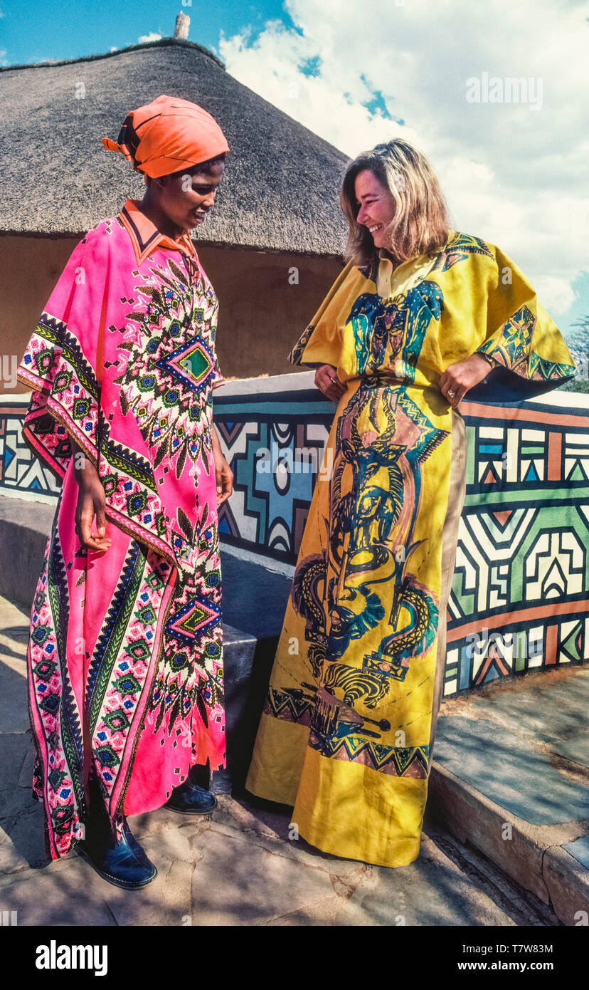 Una mujer sudafricana y una mujer americana turista admire los modernos  diseños artísticos de dos coloridos vestidos de longitud completa para la  venta en una tienda de artesanías bantú cerca de Pretoria,