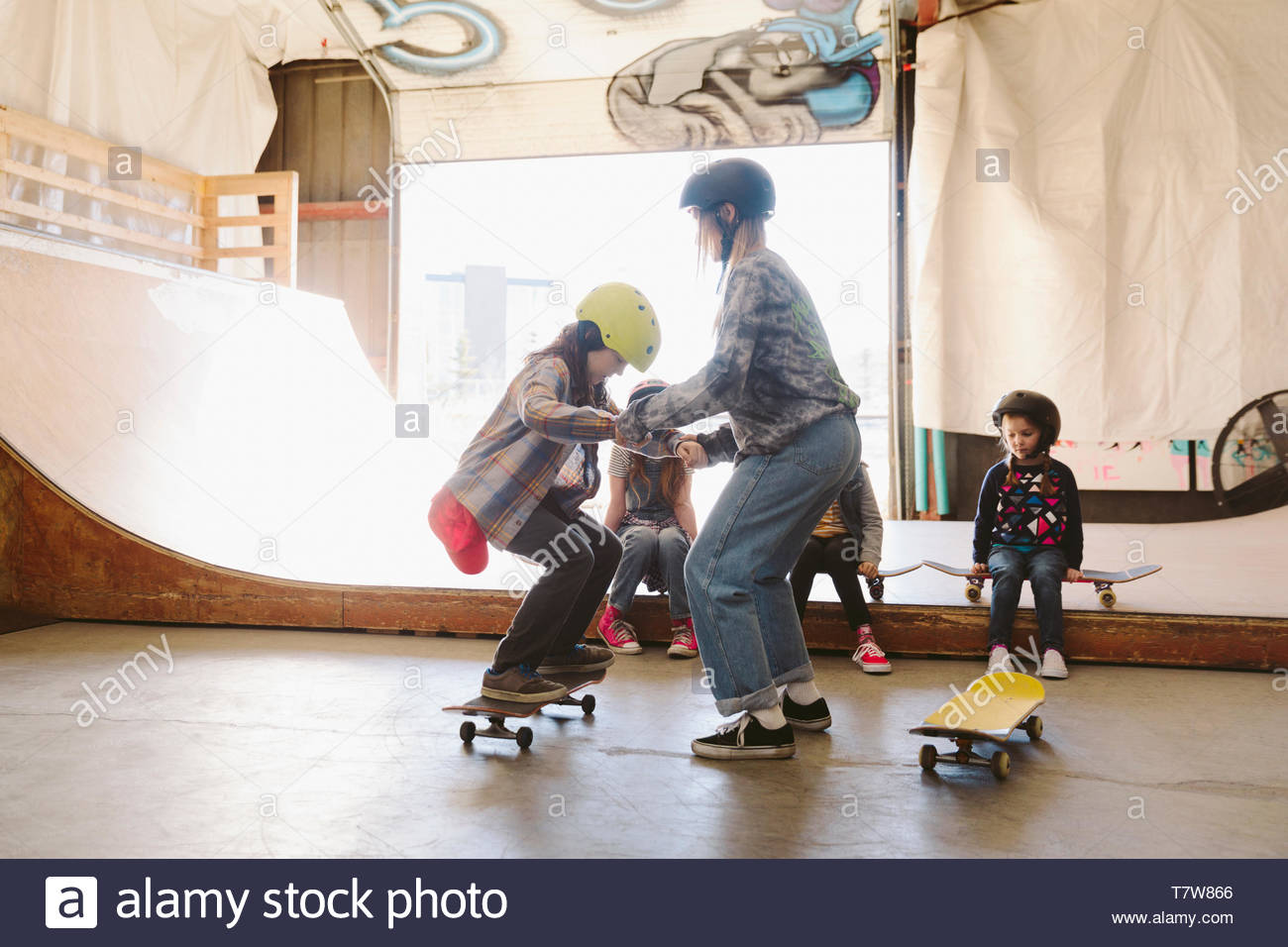 Los niños aprenden a monopatín en skate park interior Foto de stock