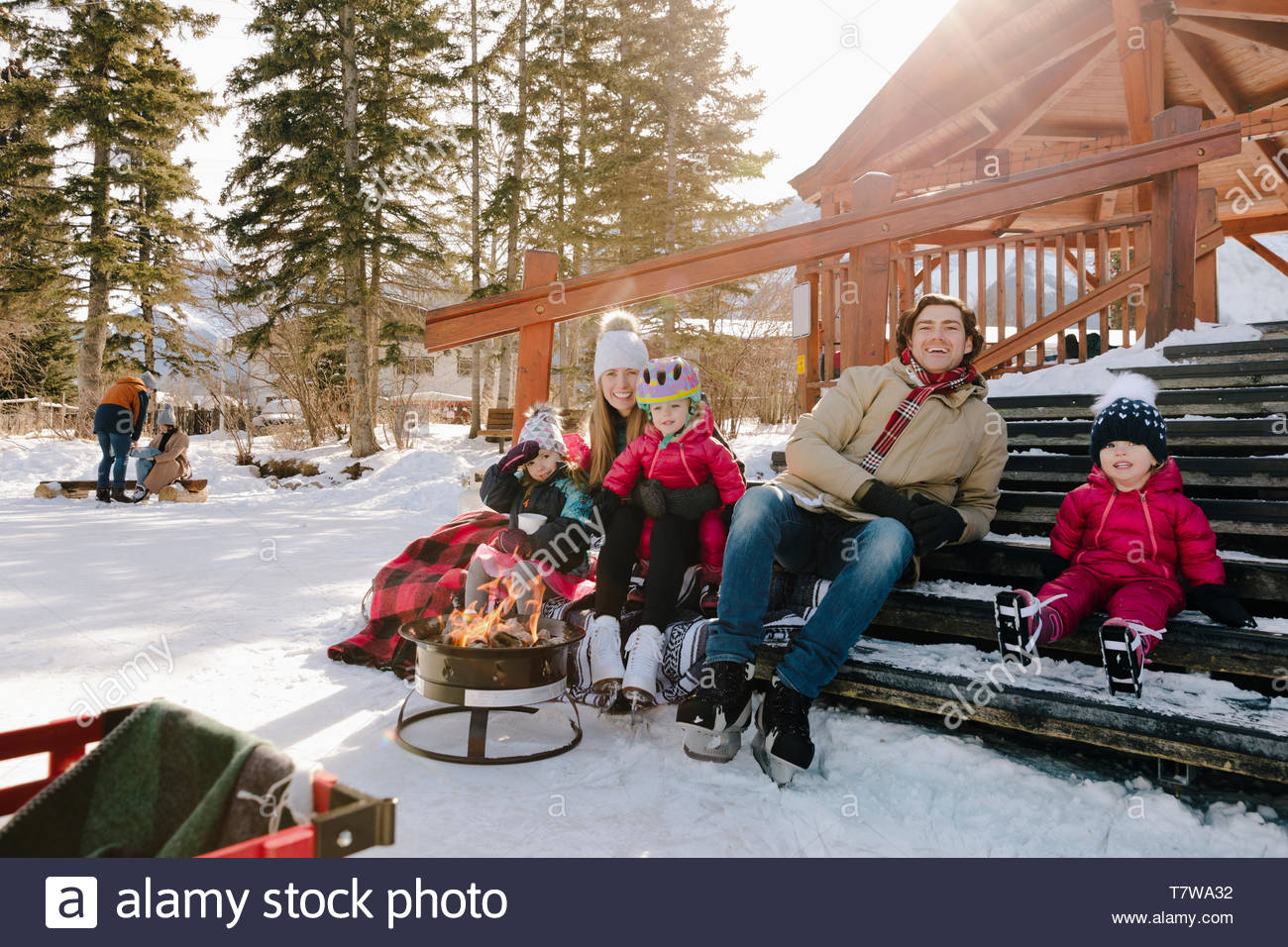 Familia Feliz tomando un descanso de patinaje sobre hielo en pasos nevados por el fuego Foto de stock
