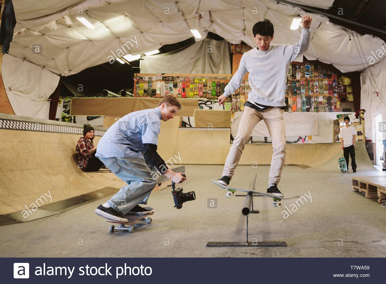 Joven con video cámara filmando amigo skateboarding en la rampa de skate park interior Foto de stock
