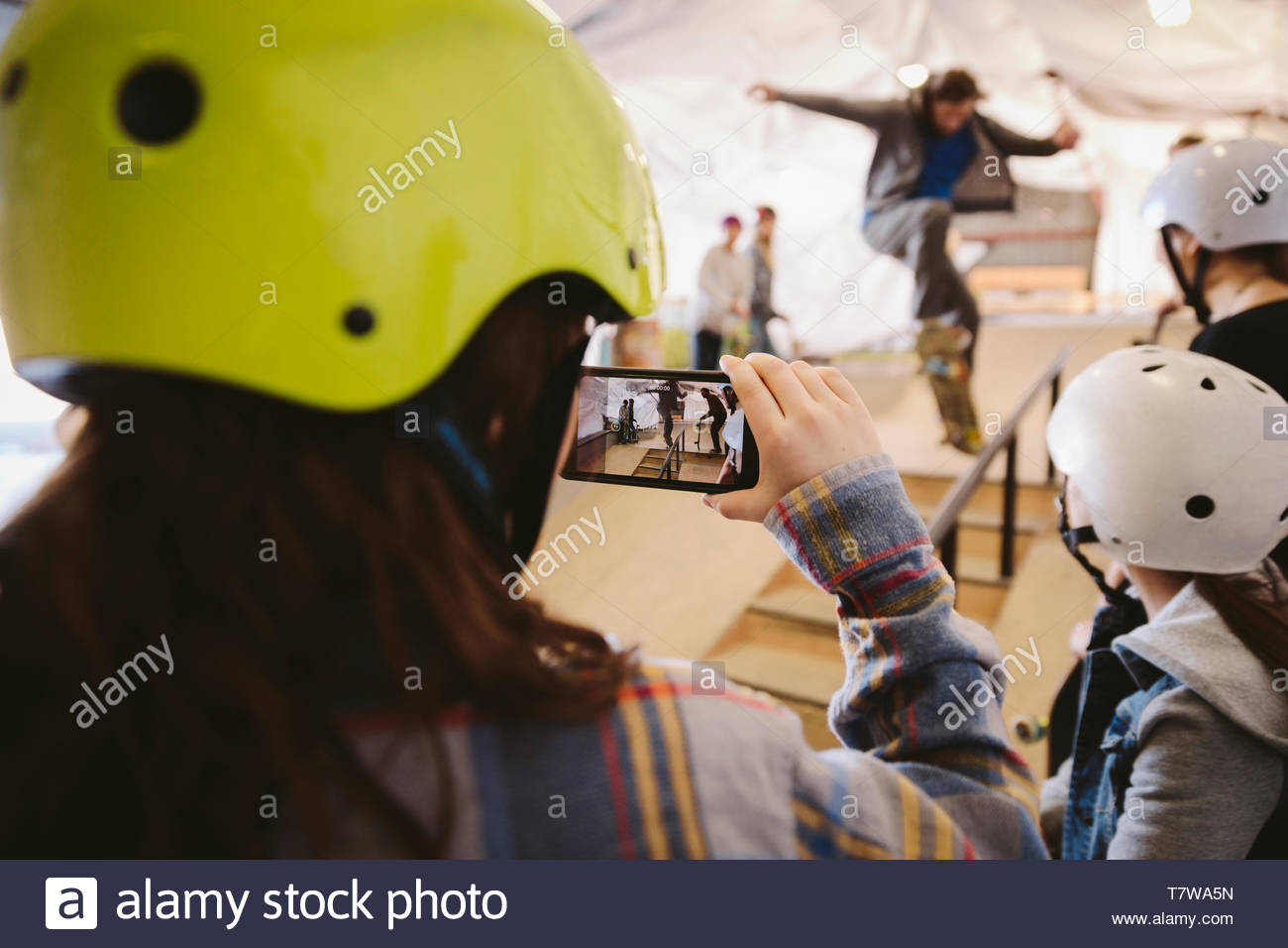 Chico con teléfono con cámara filmando el hombre de skate en el skate park interior Foto de stock