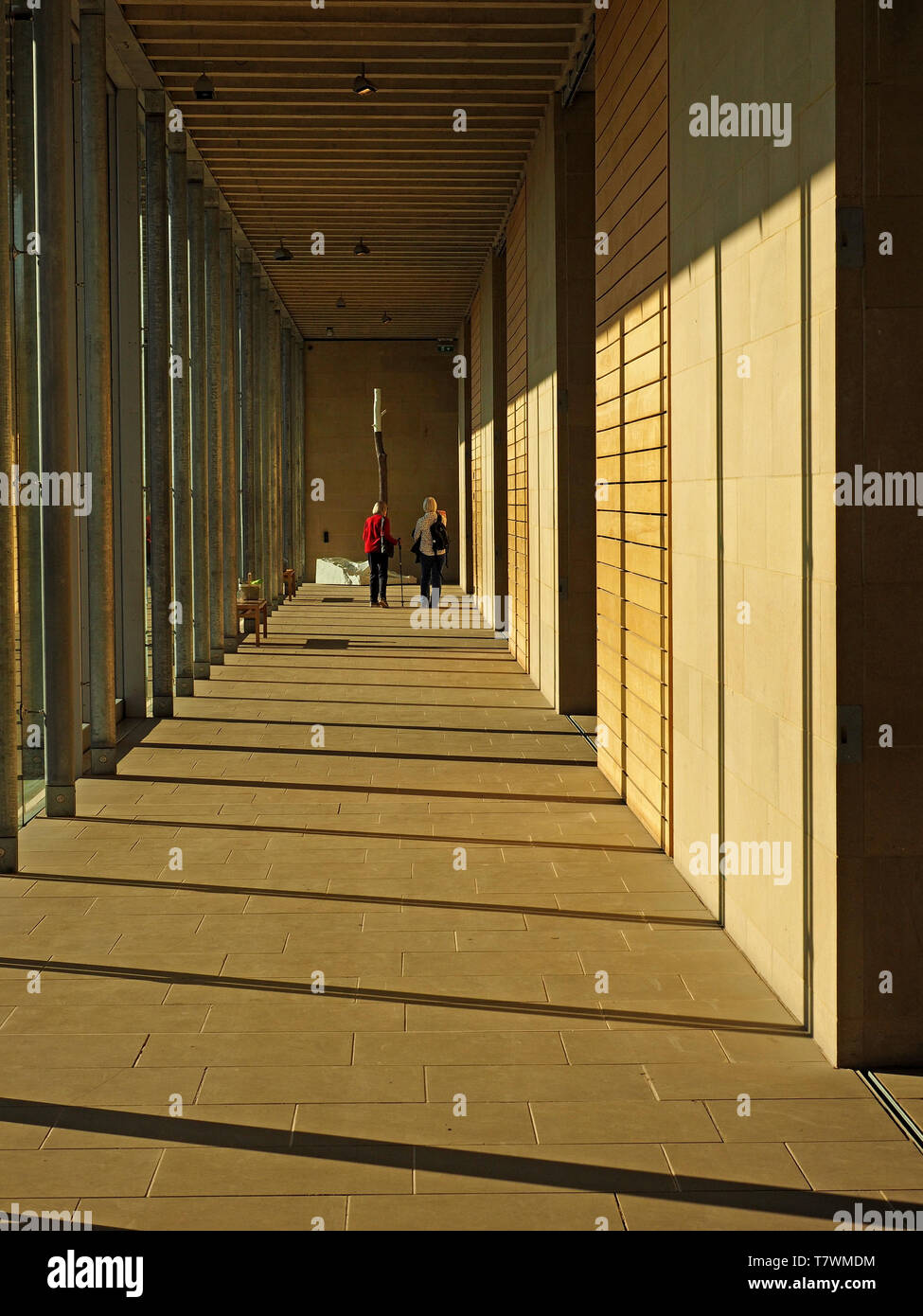 Dos figuras de incógnito al final de un pasillo acristalado con blando sombras proyectadas por la luz solar fuerte en Bretton, West Yorkshire, Inglaterra Foto de stock