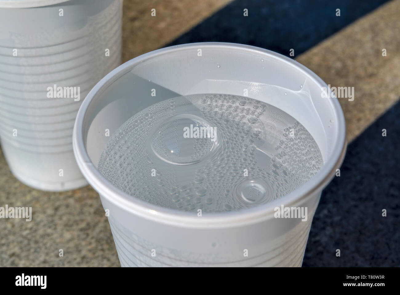 Blanco frío vaso de plástico con agua mineral con gas contra una encimera de piedra. Foto de stock